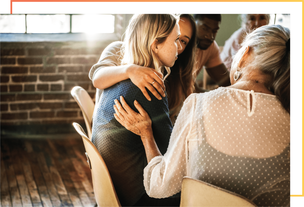 Addiction therapy program group therapy session with older woman comforting younger person