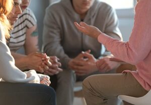 Hands of people sitting in a circle at an alcohol addiction treatment program