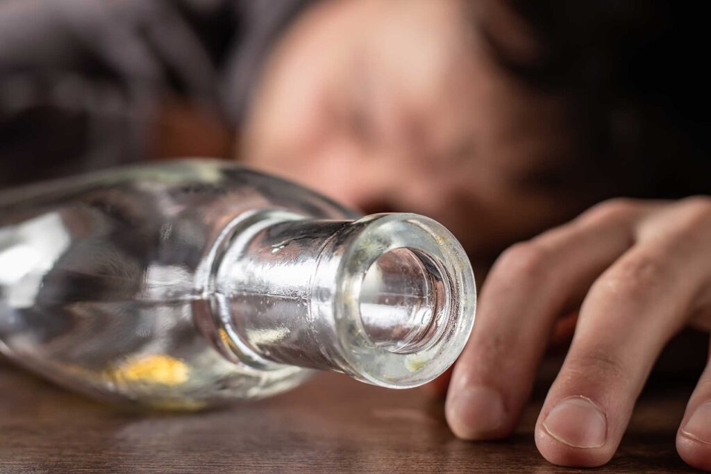 A bottle lying on its side next to the hand of a person feeling the long-term effects of alcohol abuse