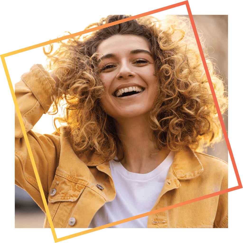 Young woman with curly hair smiling brightly, wearing a yellow jacket, framed by overlapping orange and yellow lines. Sunlight creates a warm, joyful tone.